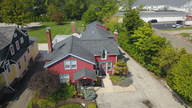 A two-story house with a red front door, a chimney, and a driveway leading to a garage. - Historic Century Home on Chardon Square (Chardon)