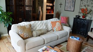 A living room with a sofa, two round wicker ottomans, a bookshelf, a potted plant, and a fireplace. - Historic Century Home on Chardon Square (Chardon)