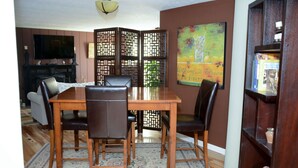 A dining area with a wooden table and chairs, a decorative screen, a television, and a bookshelf. - Historic Century Home on Chardon Square (Chardon)
