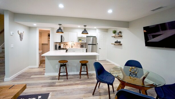 A modern kitchen with a central island, bar stools, and a dining area with a glass table and blue chairs. - Cozy Remodeled Apt Home w/Patio & Great Location (Austin)