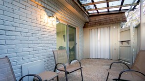 A covered patio area with brick walls, a glass door, and metal chairs. - Cozy Remodeled Apt Home w/Patio & Great Location (Austin)