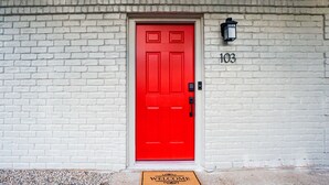 A red door with a white brick wall, a welcome mat, and a number '103' above the door. - Cozy Remodeled Apt Home w/Patio & Great Location (Austin)