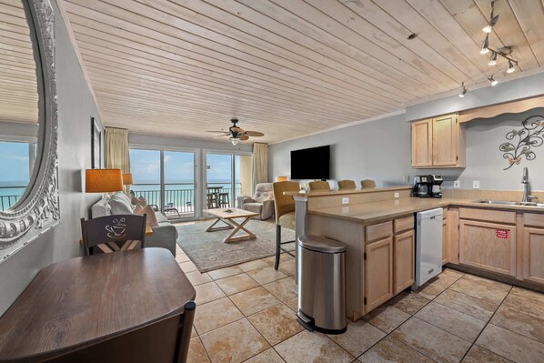 A modern kitchen with a central island, a dining area with a table and chairs, and a living area with a sofa and a TV.
