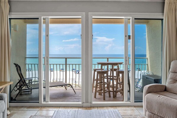 A balcony with a view of the beach, a lounge chair, and a bar area.