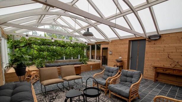 Une pièce de style serre, avec un haut plafond, des murs en bois et un espace salon comprenant des canapés et des fauteuils.