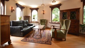 Un salon spacieux avec un canapé en cuir, une table basse en bois et un fauteuil vert. De grandes fenêtres à arc surmontent une commode en bois.