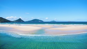 A beach with clear turquoise water, sandy shores, and distant mountains.