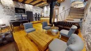 A rustic interior with exposed stone walls, a wooden floor, a leather sofa, and a staircase.