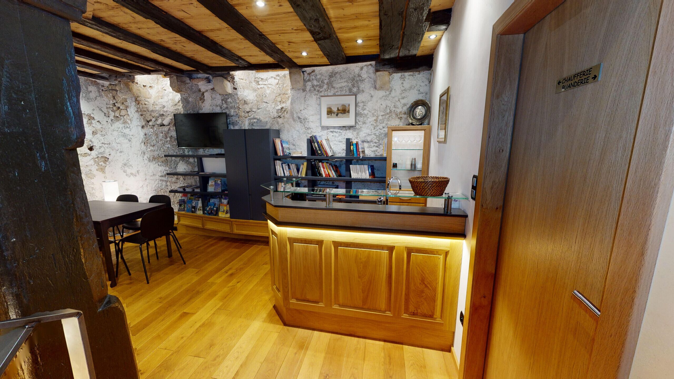 Une cuisine rustique avec des murs en pierre apparentes, des poutres en bois, une bibliothèque intégrée et un comptoir en bois doté d’un évier.