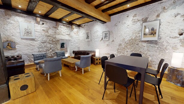 A rustic room with exposed brick walls, wooden beams, a leather sofa, a wooden coffee table, and a dining table with chairs.