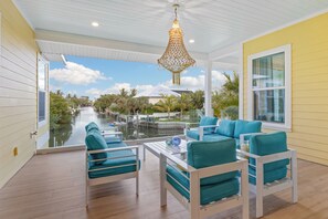 A covered outdoor seating area with teal upholstered chairs and a hanging light fixture. - Yellowfin Inn: Luxury canal-front, pool home on Anna Maria Island (Anna Maria)