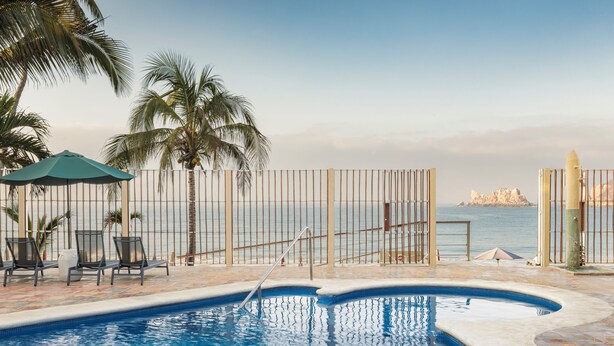 A pool area with chairs and a palm tree, a fence, and a view of the sea. - Las Arenas Bungalows Melaque (San Patricio Melaque)