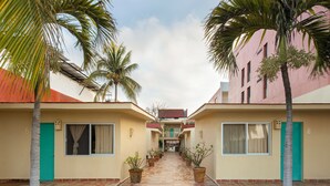 A corridor with potted plants, a green door, and a building with a red roof. - Las Arenas Bungalows Melaque (San Patricio Melaque)