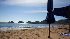 A beach with a sandy shore, a clear blue sky, and a few umbrellas. - Las Arenas Bungalows Melaque (San Patricio Melaque)