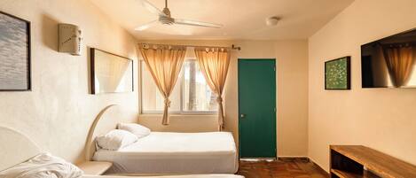 A room with two beds, a ceiling fan, a green door, and a wooden bench.