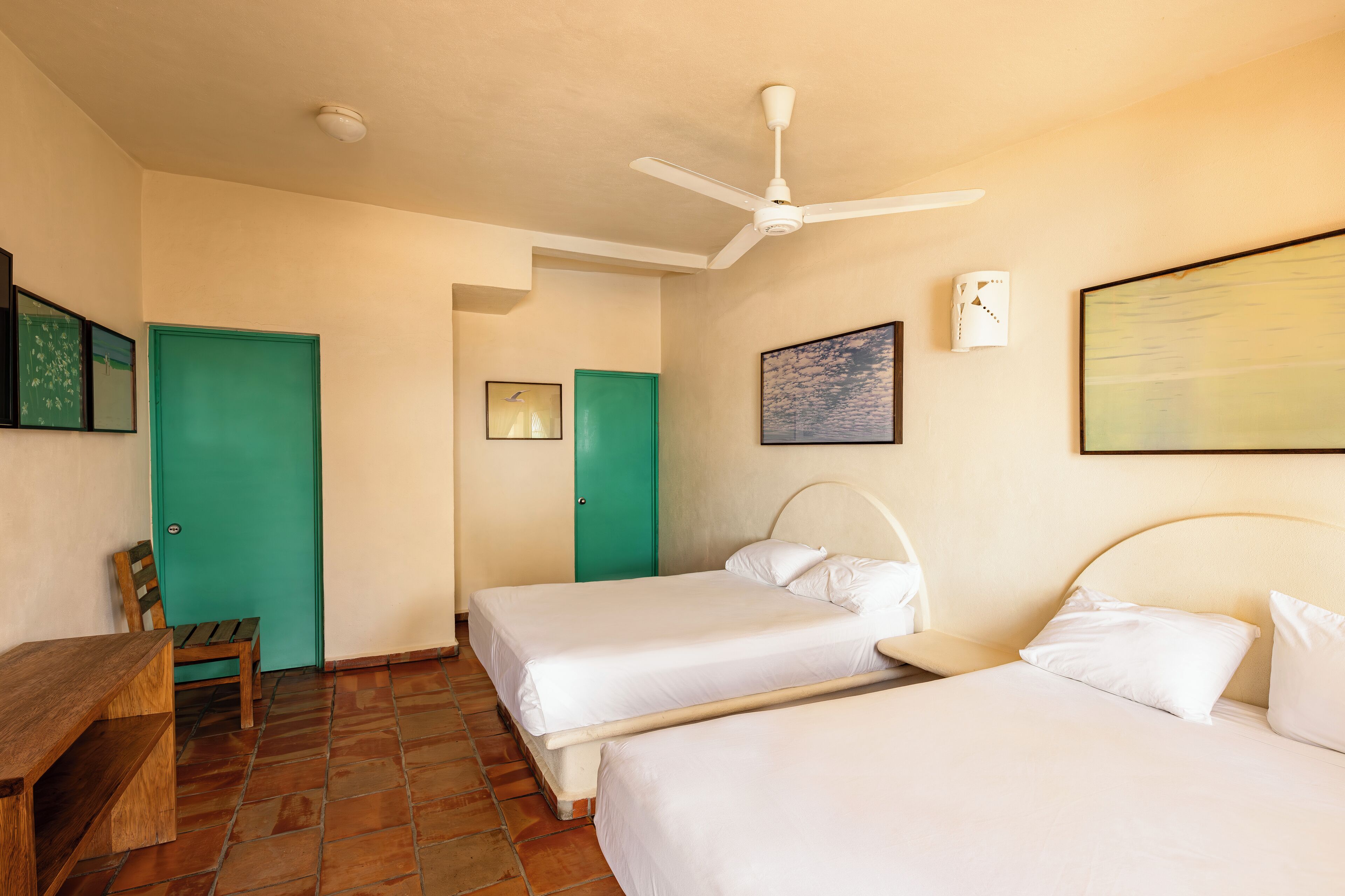 A room with two beds, a ceiling fan, a green door, and a wooden bench.