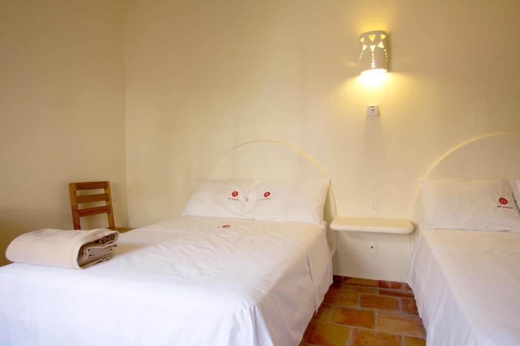 A hotel room with two single beds, a wooden chair, a nightstand, and a wall-mounted light fixture.