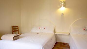 A hotel room with two single beds, a wooden chair, a nightstand, and a wall-mounted light fixture.