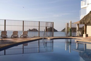 Piscina com vista para o mar, estrutura com telhado de palha e área cercada com cadeiras.