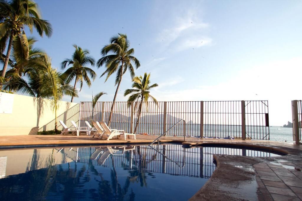 A swimming pool with lounge chairs and palm trees, surrounded by a fence.