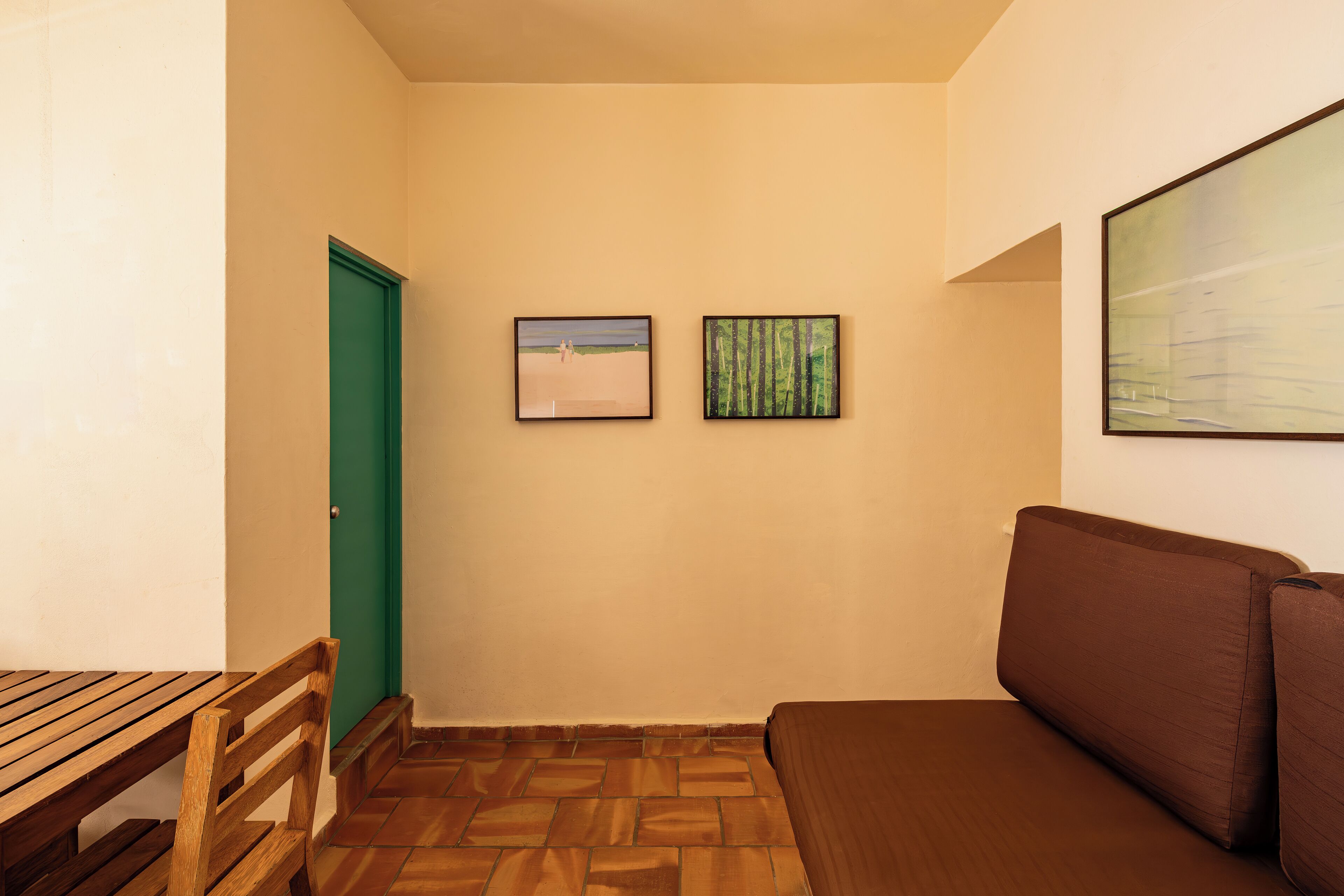 A room with a wooden bench, a green door, a brown sofa, and two framed pictures on the wall.