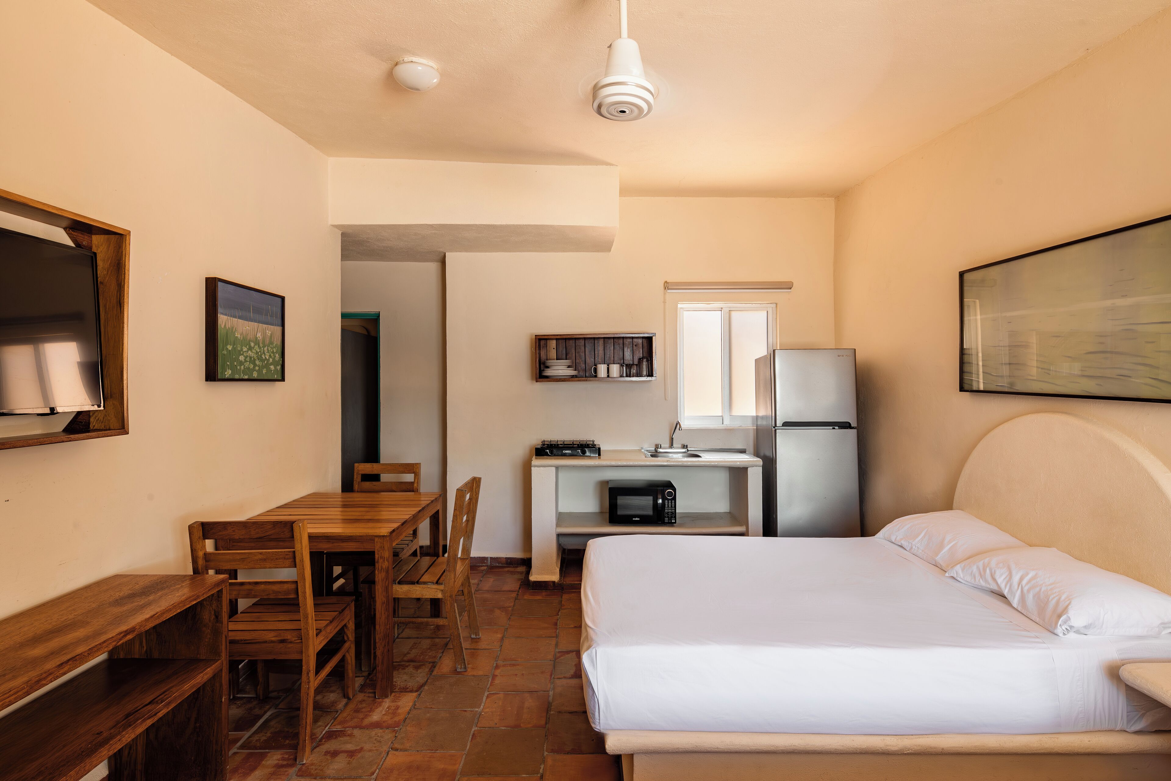 Habitación pequeña con una cama, un escritorio con computadora, un microondas y un refrigerador.