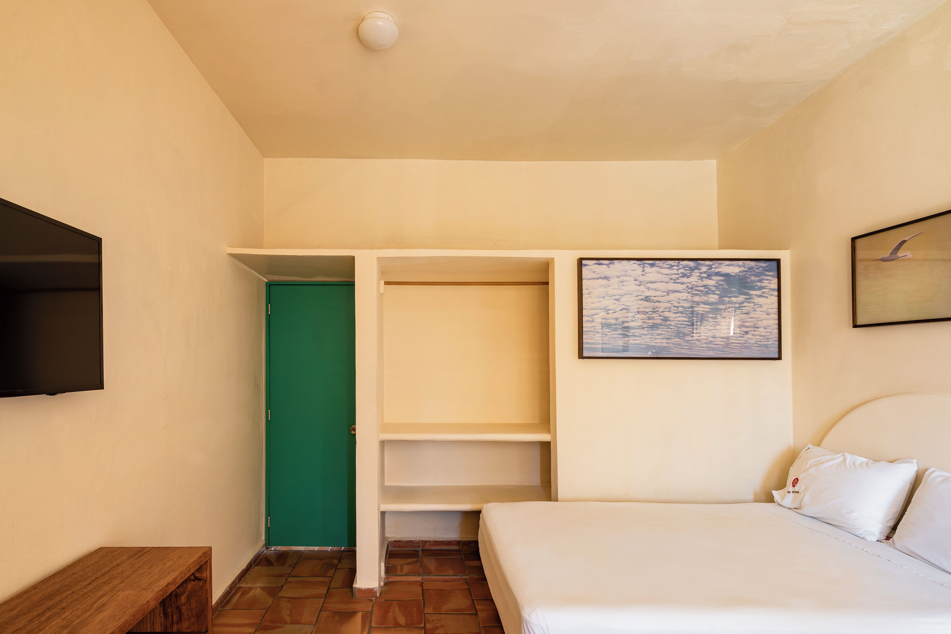 A bedroom with a bed, a green door, a wardrobe, and a painting on the wall.