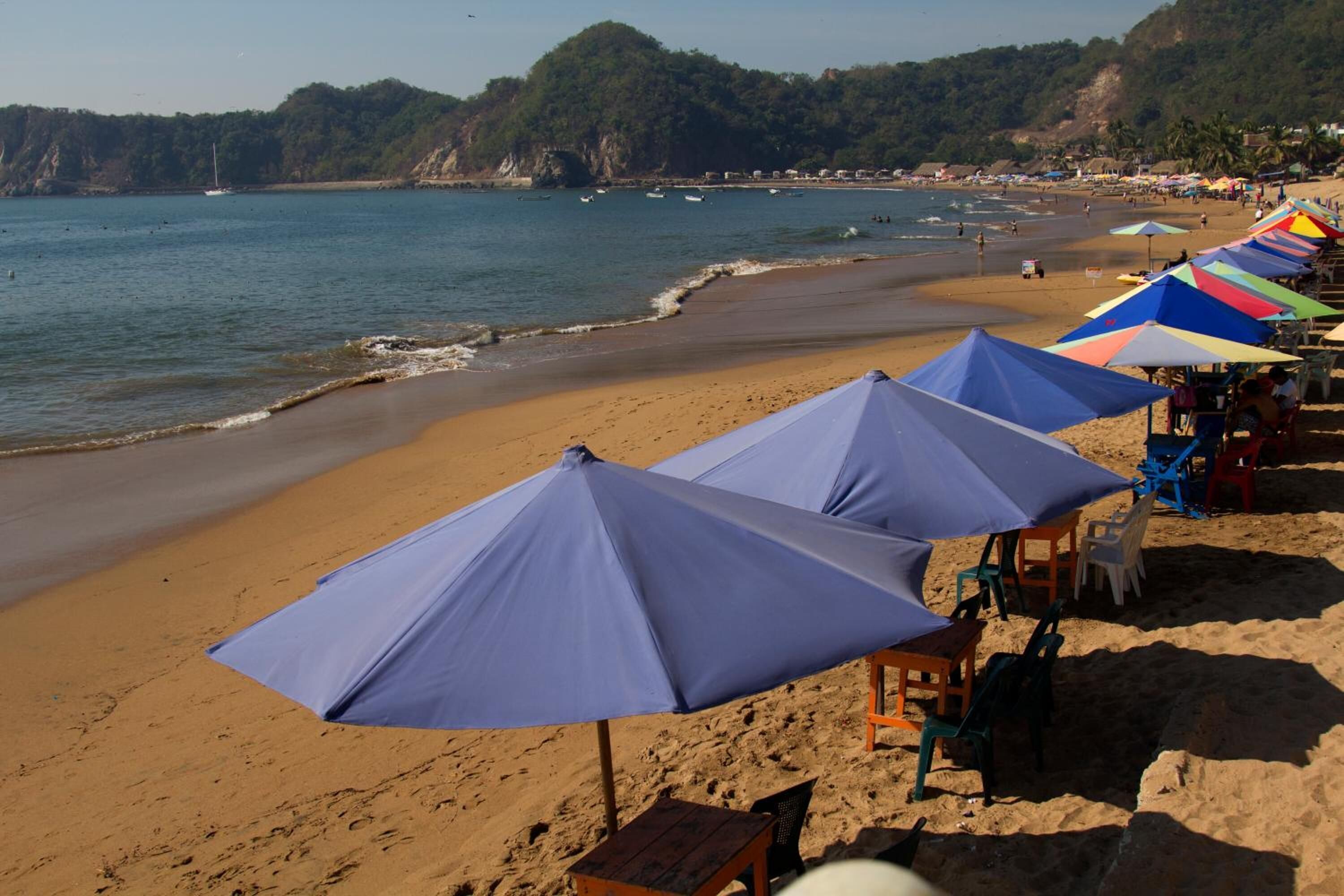 A beach with umbrellas and chairs, a sandy shore, and boats in the water.