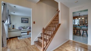 Un vaste espace de vie comprenant un escalier en bois, un ensemble de canapés et un coin repas avec des chaises.