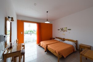 Un dormitorio con dos camas, una mesa de madera, un escritorio y un balcón con vistas.