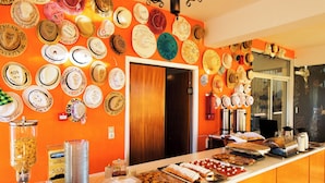 A buffet area with a variety of food items and a wall decorated with numerous hats. - Laura (Kos)
