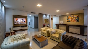 A modern living room with a flat-screen TV, two beige sofas, a coffee table, and a black sofa. - Tambaú Beach Hotel (João Pessoa)