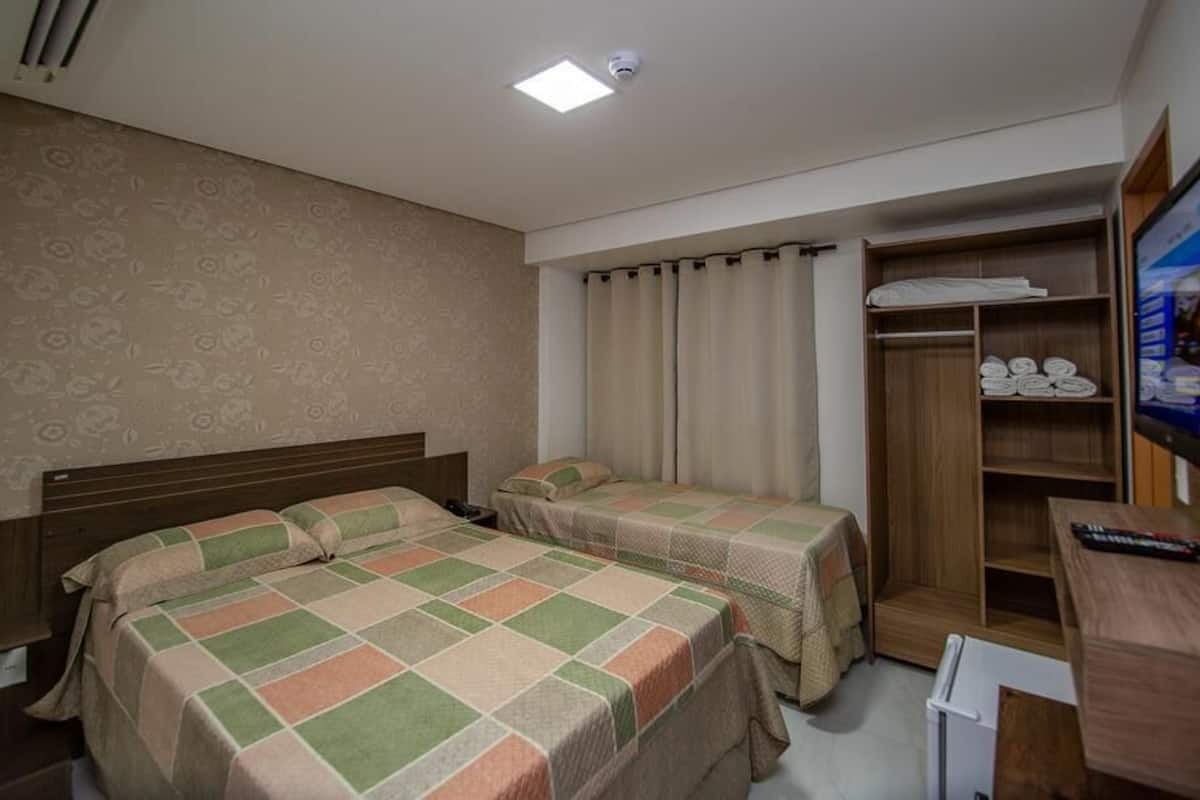 A hotel room with two beds, a wardrobe, a desk, and a television.