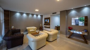 A modern living room with a sofa, two armchairs, a coffee table, and a TV mounted on the wall. - Tambaú Beach Hotel (João Pessoa)