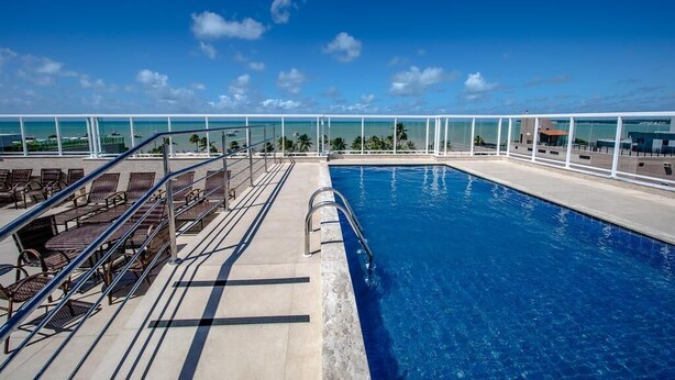 A pool area with lounge chairs and a clear view of the ocean. - Tambaú Beach Hotel (João Pessoa)