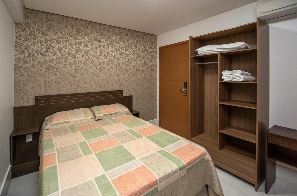 Een slaapkamer met een bed, een houten garderobe en een behang met patroon.