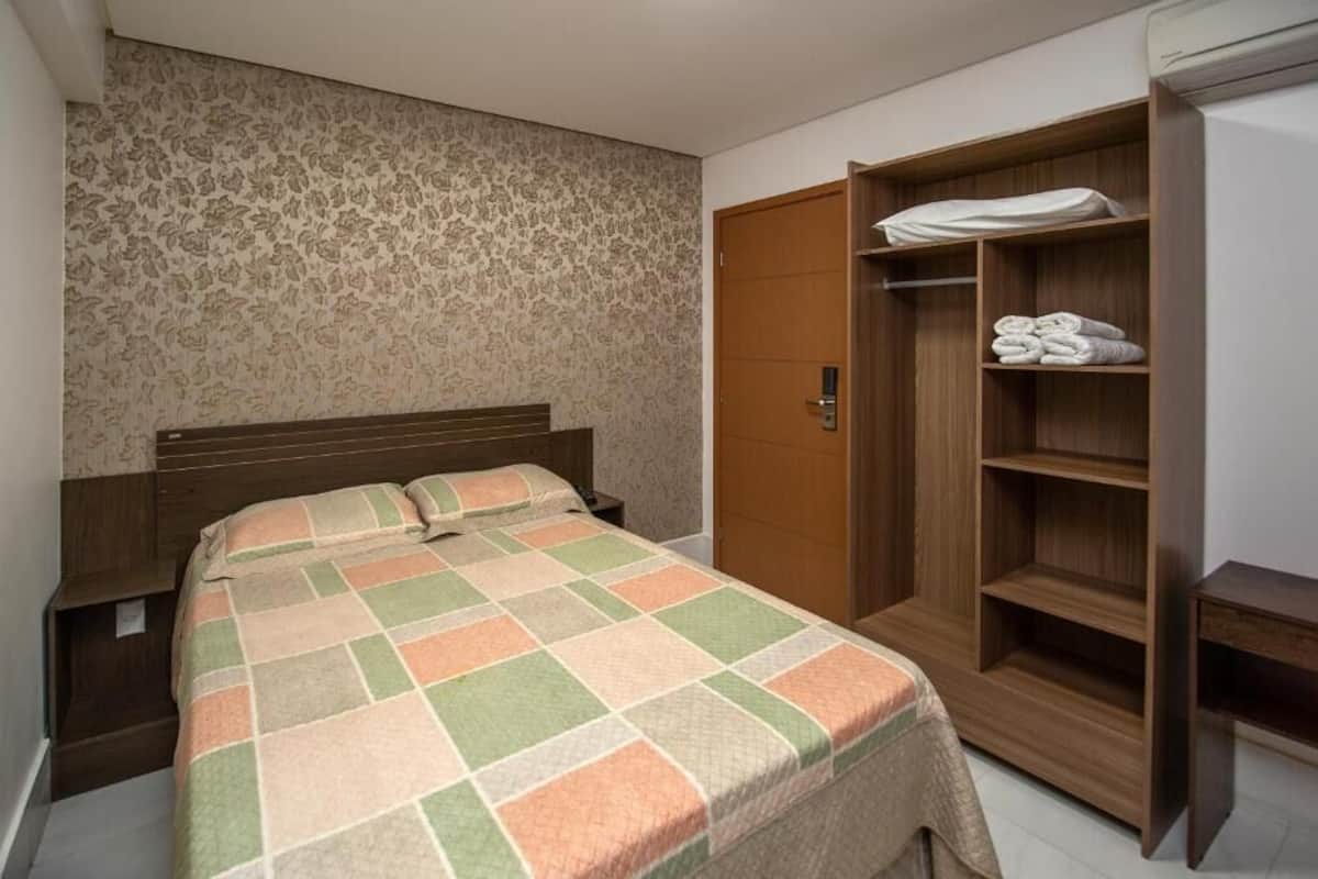 A bedroom with a bed, a wooden wardrobe, and a patterned wall.