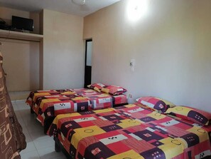 A hotel room with three beds, each with colorful quilts, a television on a shelf, and a door to the right. - Casa Hotel Mar y Paz By Rotamundos (Úrsulo Galván)
