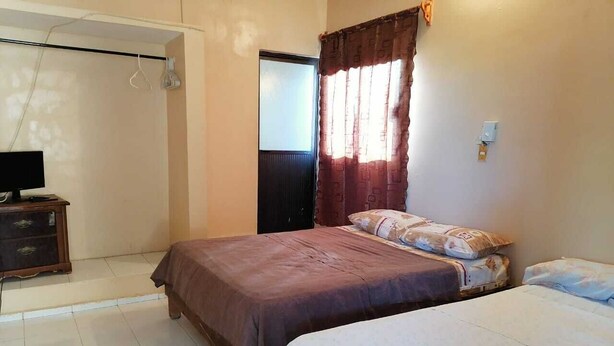 Habitación con dos camas, un armario, un televisor y una ventana con cortinas.