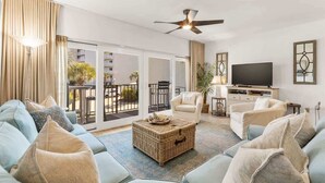 A spacious living room with a sofa, armchairs, a TV, and a balcony with a view. - Swell Life - Private Beach- 4 Bikes (Santa Rosa Beach)