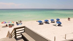 A beach with a wooden deck, several beach umbrellas, and lounge chairs. - Swell Life - Private Beach- 4 Bikes (Santa Rosa Beach)