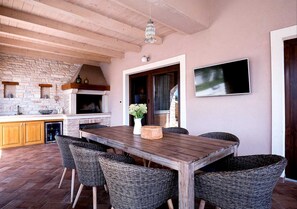 An outdoor dining area with a wooden table and wicker chairs, a brick fireplace, and a stone wall. - Villa Ambienta with Heated Pool (Krnica)