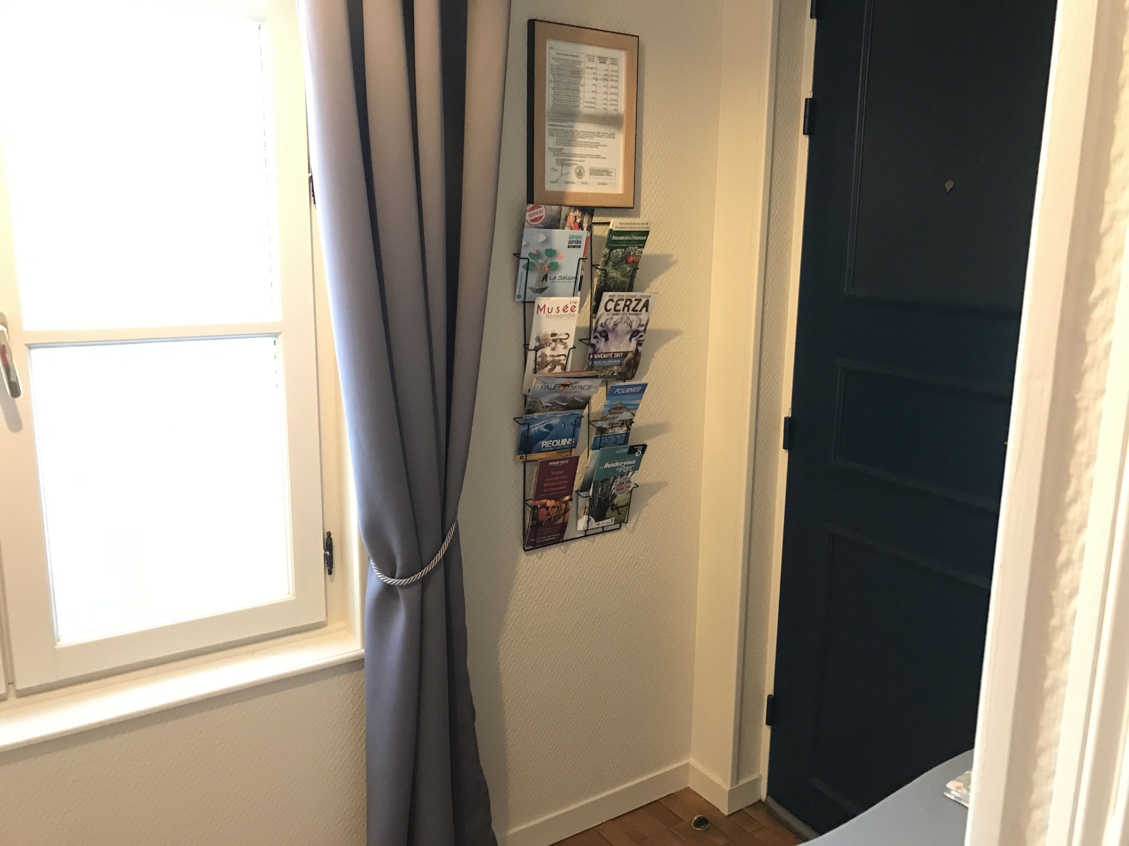 A room with a window, a curtain, a wall-mounted bulletin board with various items, and a door.