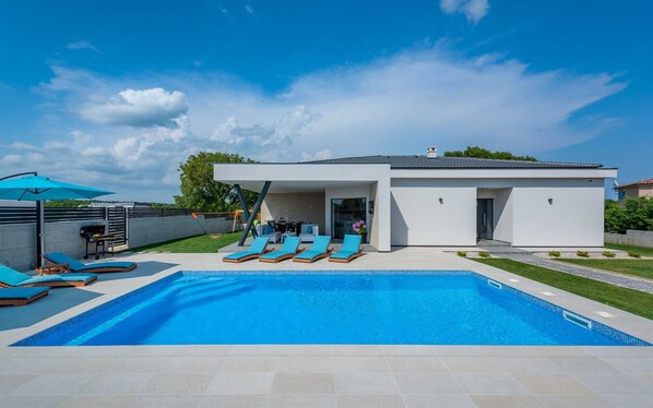 A modern house with a swimming pool, outdoor seating, and a patio area.