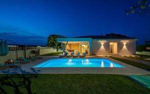 A modern house with a swimming pool, outdoor seating, and a well-lit entrance.