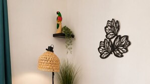 Un salon avec un téléviseur, une table colorée à rayures, une lampe sur pied, une sculpture noire et une petite étagère avec une plante.
