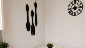 Un coin repas avec une table blanche, quatre chaises, deux plantes en pot et une horloge fixée au mur.
