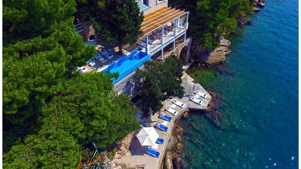 An aerial view of a coastal property with a swimming pool, a covered deck, and lounge chairs along the shoreline. - Villa Dubrovnik Secret Escape with Pool (Dubrovnik)