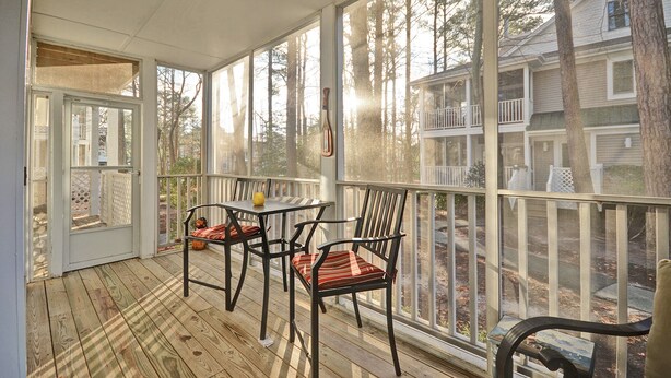 En inglasad veranda med ett bord och stolar, stora fönster och utsikt över ett bostadsområde.