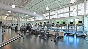 Ett gym med flera löpband och motionscyklar, stora fönster och ett högt tak.